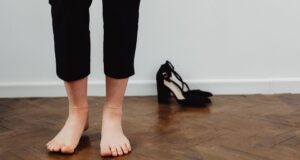 Blote voeten op een houten vloer naast zwarte schoenen met hakken