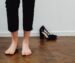 Blote voeten op een houten vloer naast zwarte schoenen met hakken